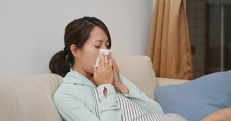 Sick woman sneeze and sit on sofa at home