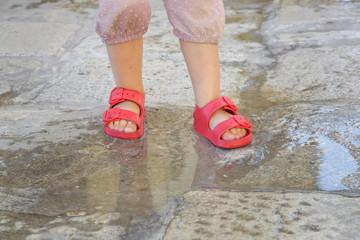 Child feet in red rubber sandals jumping into a puddle of rain