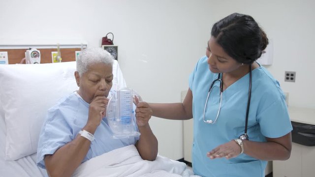 Nurse helps female patient with spirometer in hospital patient room