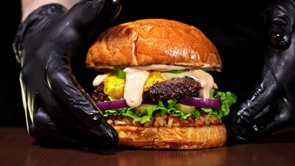 Craft burger is cooking on black background. Consist: sauce salsa, lettuce, red onion, pickle, cheese, chilli green pepper, bun, marbled meat beef.