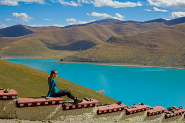 Young female traveler sits on a ledge overlooking turquoise colored Yumtso lake.