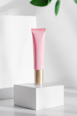 Natural foundation cream tube mock up side view. Eco friendly cosmetology creative concept. Pink lotion container and blurred leaves composition. Organic skin care, female hygiene, makeup accessory