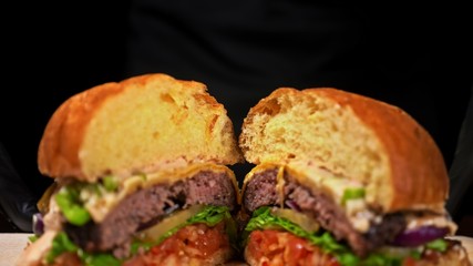 Cut craft burger is cooking on black background. Consist sauce salsa, lettuce, red onion, pickle, cheese, chilli green pepper, bun, marbled meat beef.