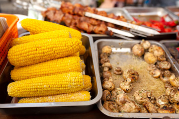 A counter with metal trays containing grilled food. Food and cooking equipment at a street food festival