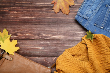 Knitted sweater with jeans, leather bag and maple leafs on brown wooden table