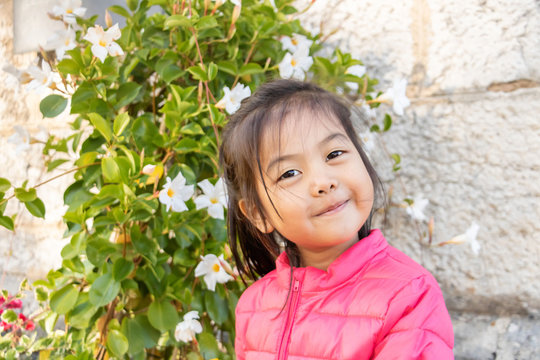 Petite fille eurasienne chinoise et fran&ccedil;aise tr&egrave;s souriante devant un bosquet en fleurs - Portrait