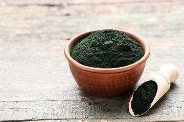 Spirulina powder in bowl and scoop on grey wooden table