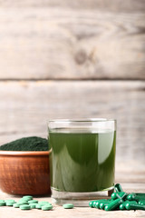 Spirulina drink and pills with powder in bowl on grey wooden table