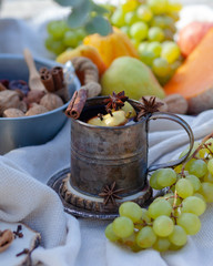 Spicy mulled wine in a metal mug decorated with clove, cinnamon, anice. Autumn, harvest time, ripe fruits as decor: grapes, pear. Rustic style. Picnic in Paris, board of Seine river, romantic and cozy