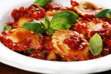 Ravioli with tomato sauce garnished with parmesan cheese and basil on rustic table