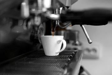 A coffee machine pours freshly brewed hot coffee into a white cup