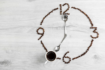 Coffee grains folded in the form of a clock on a wooden background. Instead of the number 7, a cup...