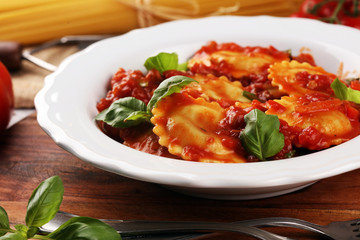 Ravioli with tomato sauce garnished with parmesan cheese and basil on rustic table