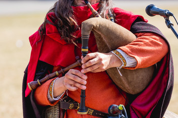 Musician in medieval clothes performs a melody on a bagpipe_