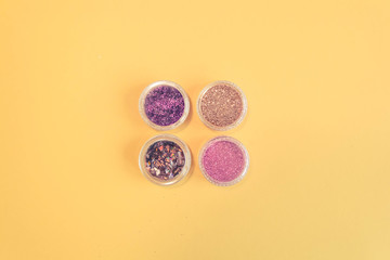 Top view of manicure and pedicure equipment on yellow background. Beauty, care and fashion concept. Professional tools for manicure. Purple, Pink and Gold Nail Glitter. Copy space