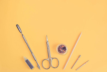 Top view of manicure and pedicure professional tools on yellow background. Beauty fashion concept. Iron and Wood Cuticle Pusher, Nails Scissors, Purple Nail Glitter, Milling Cutter Nozzles. Copy space
