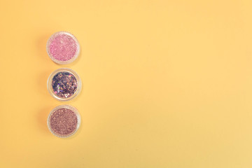 Top view of manicure and pedicure equipment on yellow background. Beauty, care and fashion concept. Professional tools for manicure. Purple, Pink and Gold Nail Glitter. Copy space