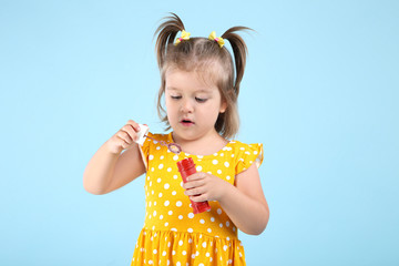 Cute little girl blowing soap bubbles on blue background