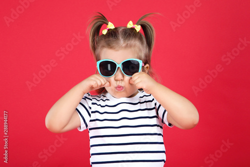 Cute little girl in sunglasses on red background