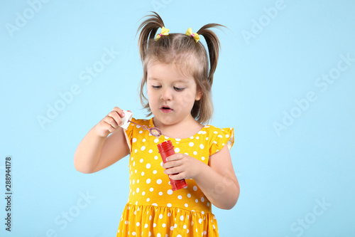 Cute little girl blowing soap bubbles on blue background