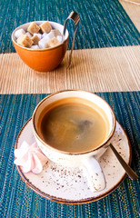 Cup of coffee in a beige ceramic cup in a cafe with meringue and pieces of sugar from cane on the table