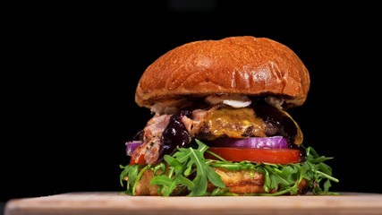 Craft burger is cooking on black background. Consist: sauce, arugula, tomato, onion, bacon, currant sauce, ricotta cheese, air bun and marble meat.