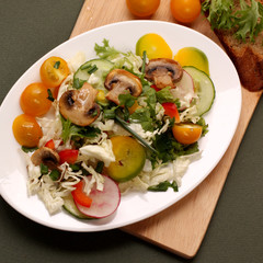 plate of salad with vegetables, herbs and mushrooms on a wooden table