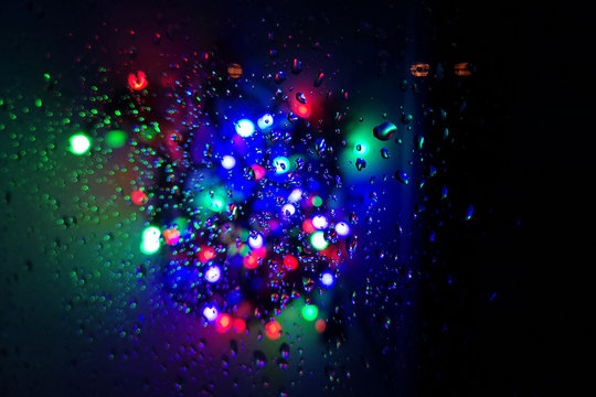 Wet window with night city background. Multicolored blurred lights. Autumn background