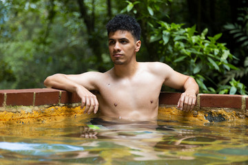 Hispanic man relaxing in natural hot springs- man in natural pool in the middle of the forest
