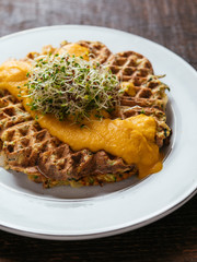 Plate with home made zucchini waffles, served with a vegan carrots based cheddar sauce.