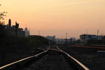 Fototapeta na wymiar railway arrow in sunset light with background of city and pink sky