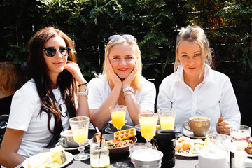 Group of friends in white having breakfast in garden at table with food and communicating, laughting concept
