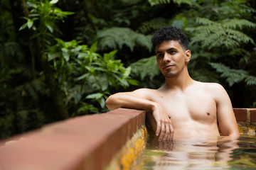 Man relaxing in natural hot springs- man in natural pool in the middle of the forest in Guatemala- Latino man in the spa...