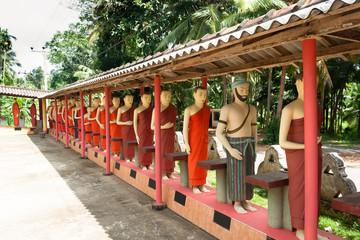 Statues of monks standing in a row behind the Buddha in one of the Buddhist temples of Sri Lanka