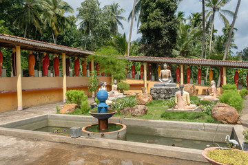 Statues of monks standing in a row behind the Buddha in one of the Buddhist temples of Sri Lanka