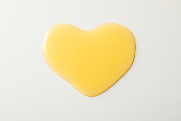 Puddle of honey in shape of heart on white background, top view