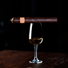 concept of alcoholism, loneliness, dependence. A glass of whiskey or cognac, a Cuban cigar on a brown wooden  table, on a black background. Elite drink for masculine relaxation