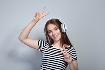 Young beautiful woman with headphones on grey background