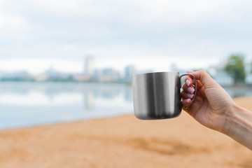 hand holding a cup of coffee or tea. morning sunlight. drinking coffee near lake in city park. sunrise time.
