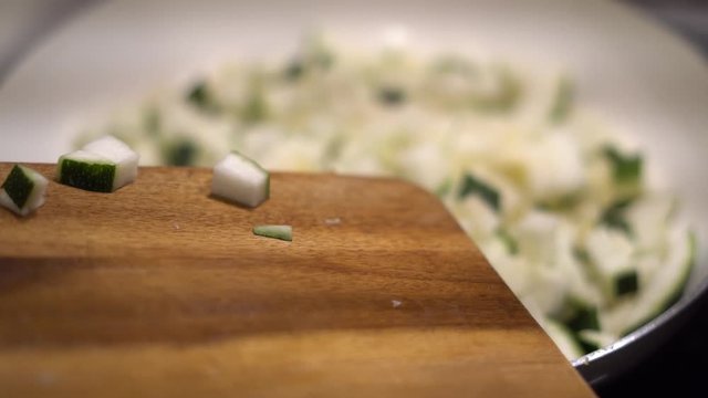 in St&uuml;cken geschnittene Zucchini  wird in Pfanne geschoben von einem Holzbrett