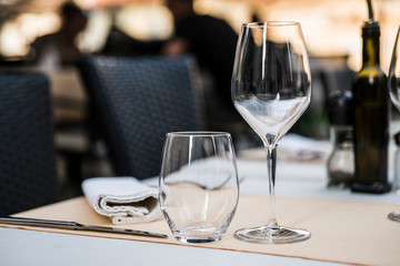 The interior of the summer restaurant. The table is served with glassware for drinks and a bottle of olive oil. Concept: preparing the table for service. Selective focus. Copy space.