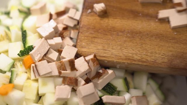 In W&uuml;rfel - Scheiben geschnittenes Tofu wird vom Brett in eine Pfanne geschoben