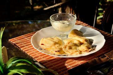 Dumplings with cottage cheese and sour cream on a table in a summer cafe, in the park on a sunny day.