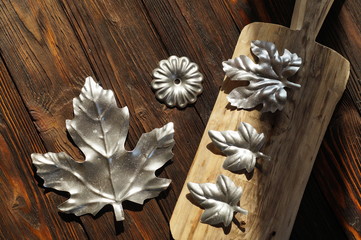 Composition of silver metal products: maple leaf large and small, flower, located on a dark wooden background and a light plate.