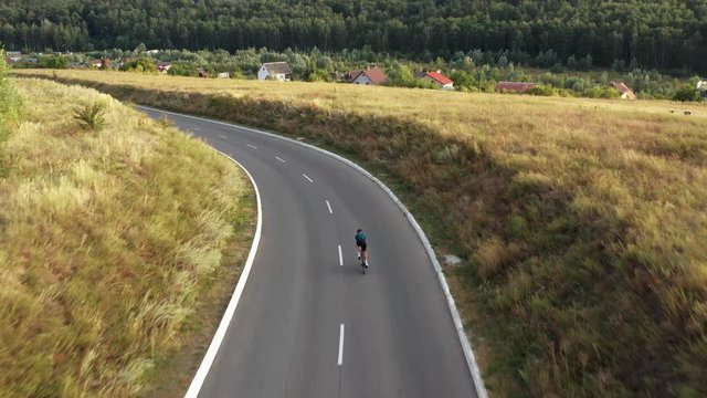 Aerial drone view of man cycling in downhill along country road.
