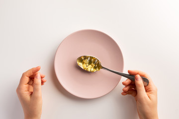 Hands with spoon of fish oil capsules. Flat lay.