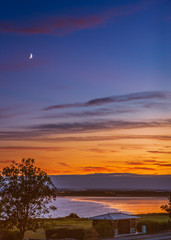 A new moon above Sandwich Bay as the golden sunset reflects into the low tide of the bay.