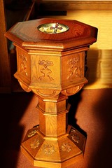 Sunbeams streaming in on old traditional eight sided wooden baptismal font with crucifix depicting...