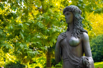 Fototapeta na wymiar The statue of Flora in Paradise Park on a background of green leaves
