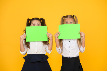 Wow. Little girls holding empty sheets of paper on yellow background. Small children with blank green school paper for assignment or project work. Examination paper. Academic paper, copy space